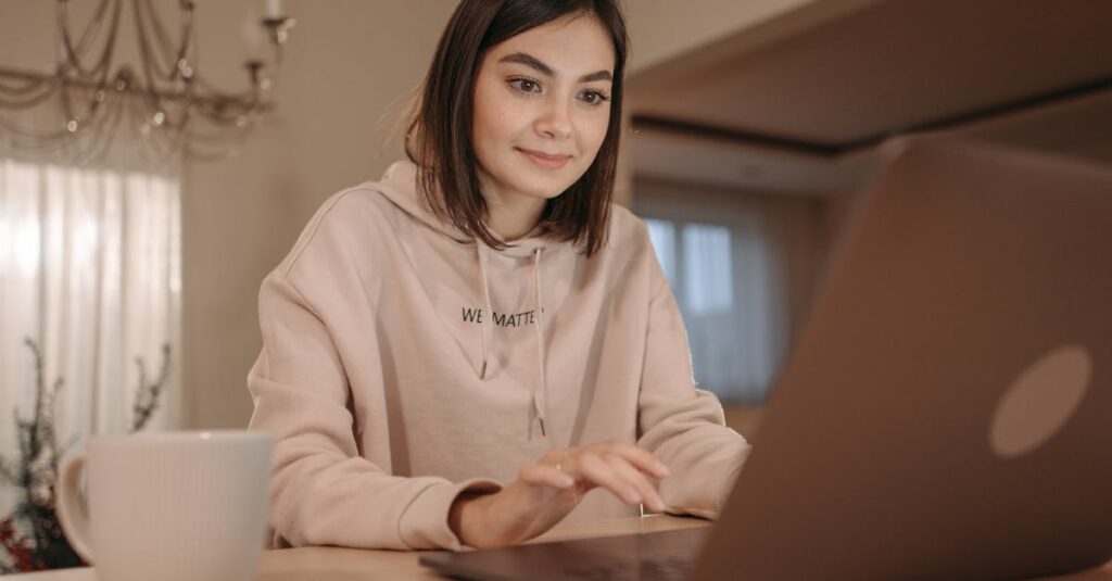 A young woman in a cozy setting using a laptop with a cup of coffee nearby.